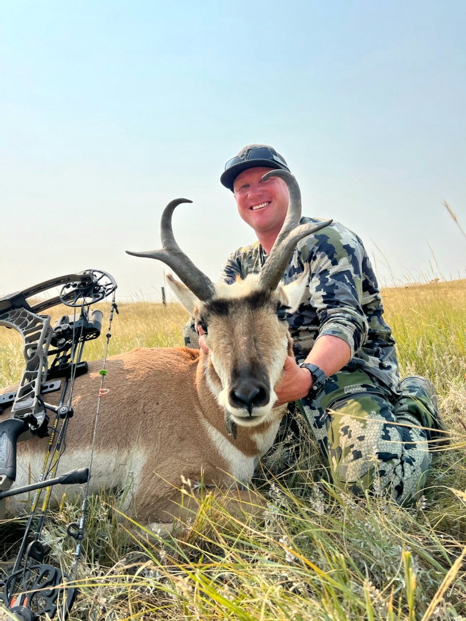 Hunter with harvested antelope and compound bow in open prairie