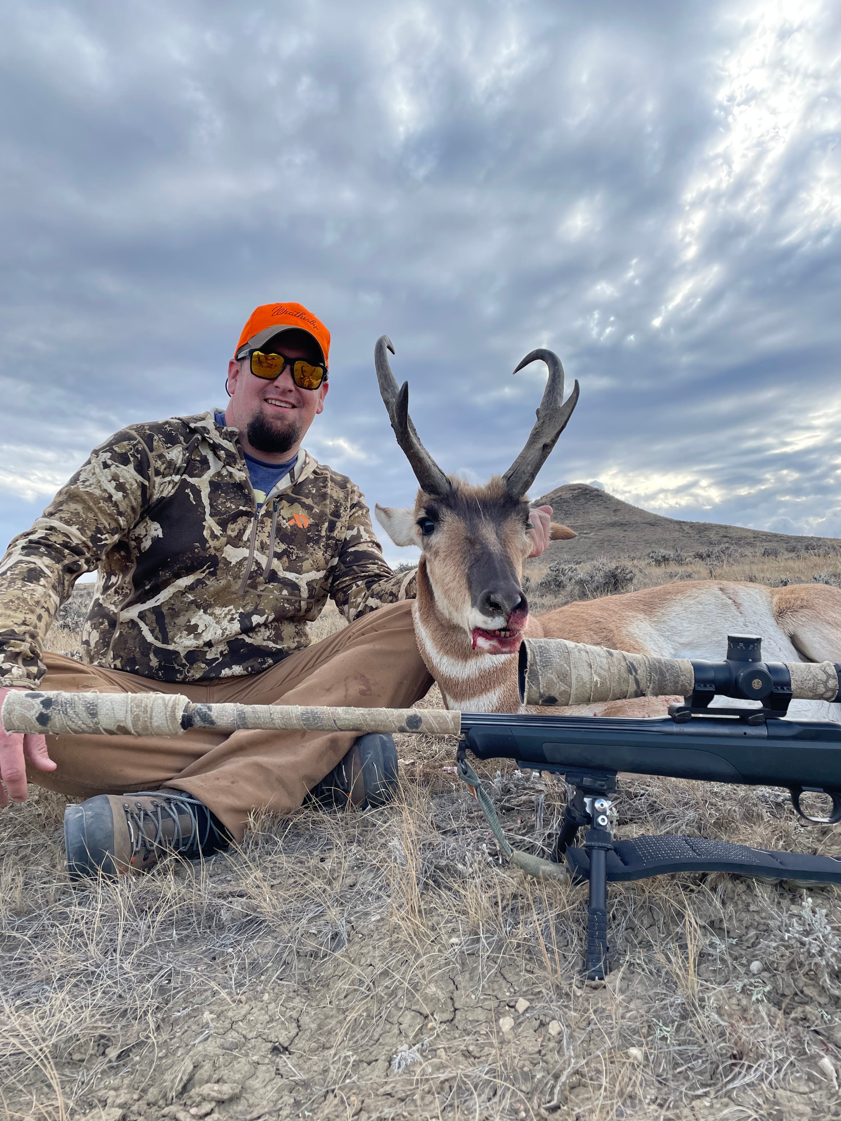 Hunter with antelope and rifle in camo, orange hat