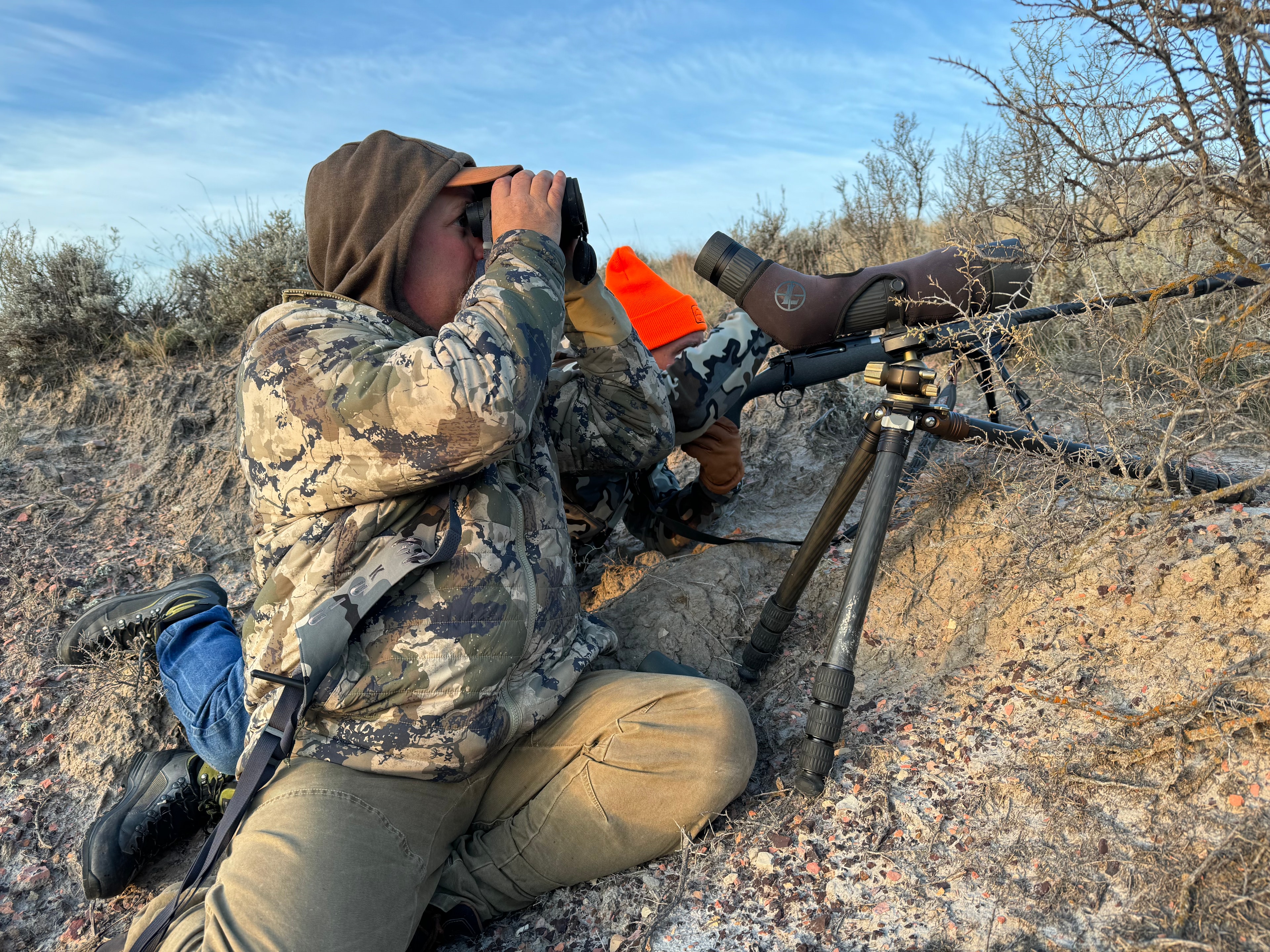Two hunters glassing with binoculars and spotting scope on tripod