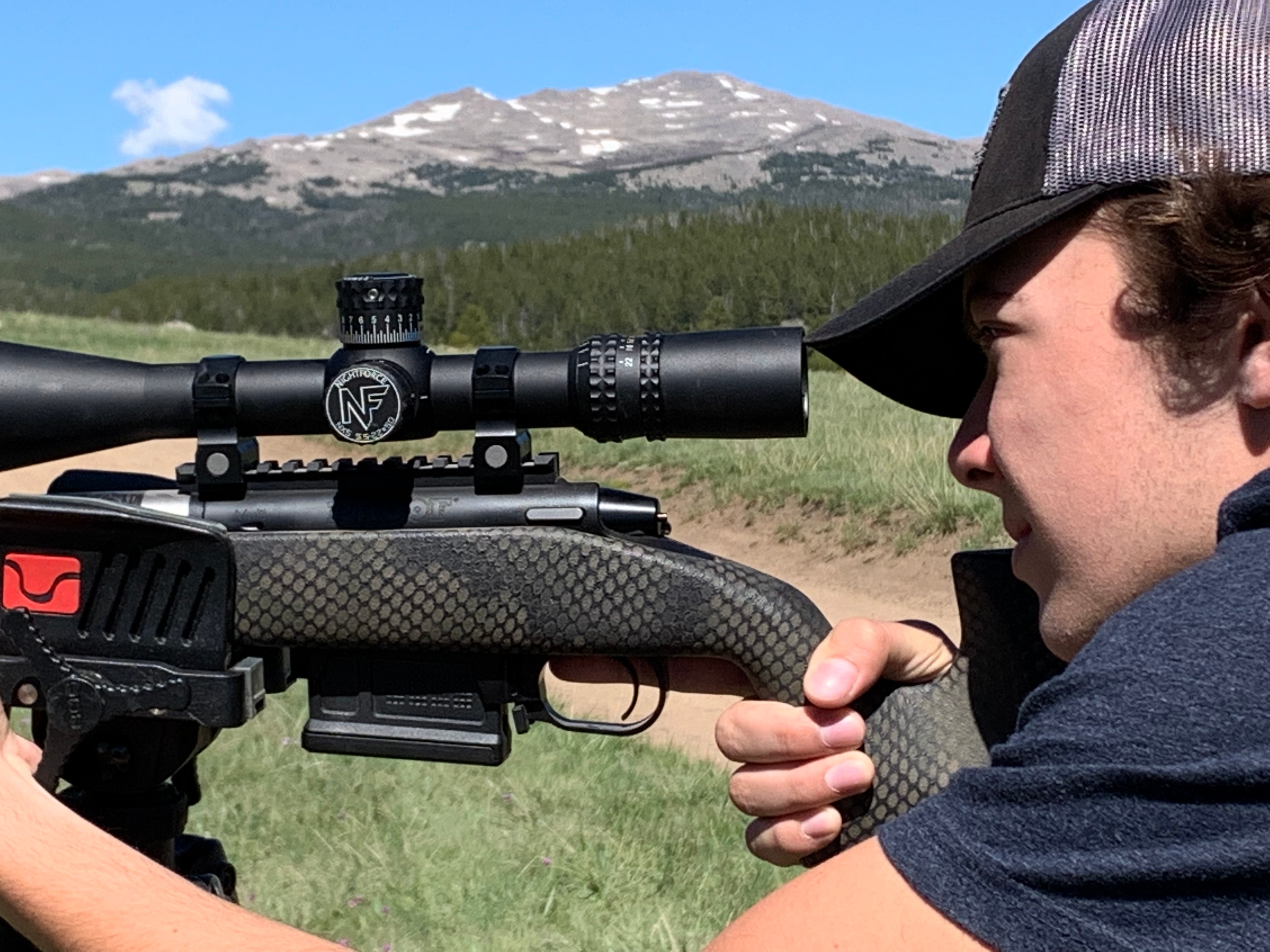 Young hunter aiming Nightforce scoped rifle with mountain backdrop