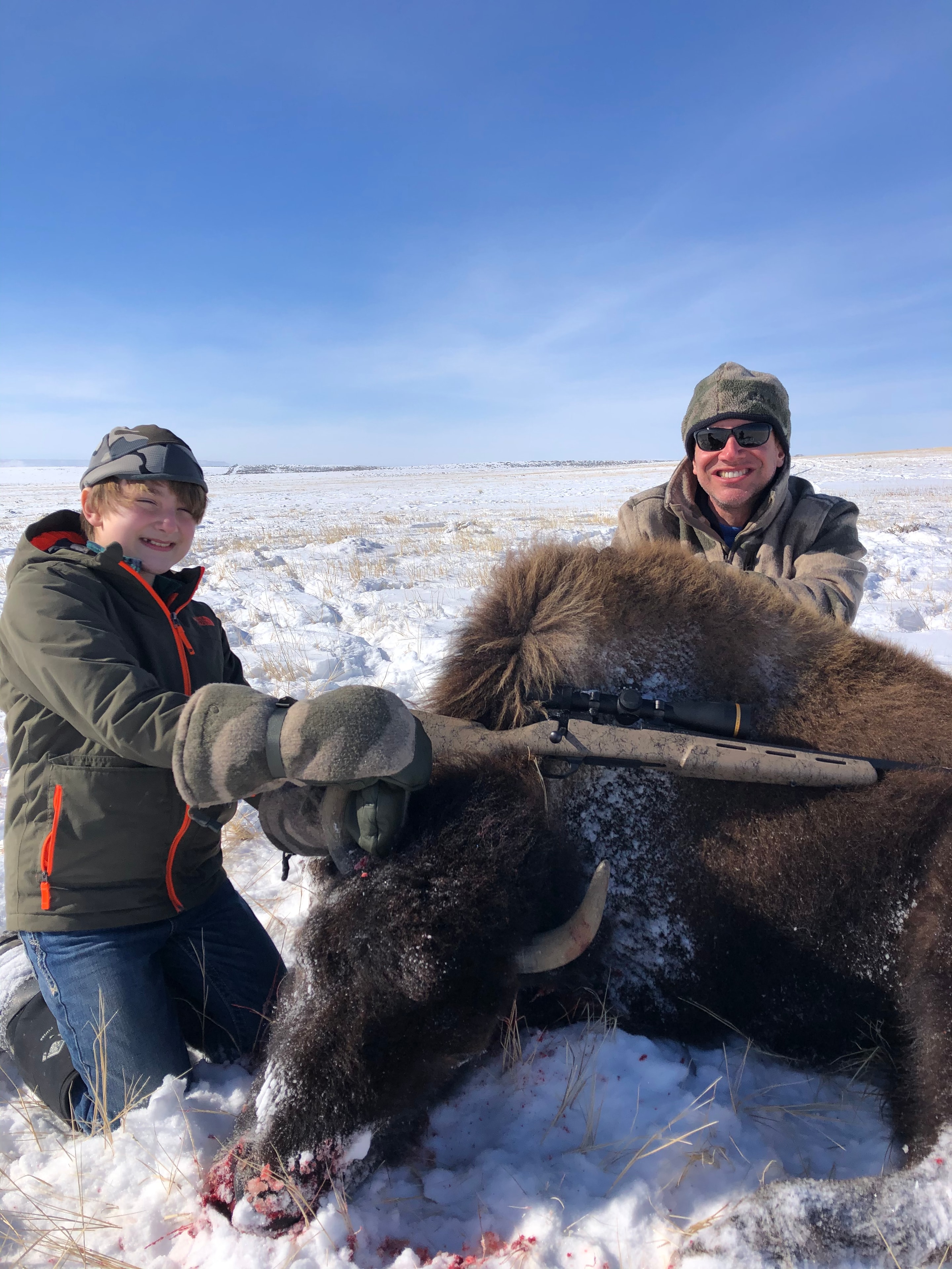 Two hunters with harvested bison in winter snow