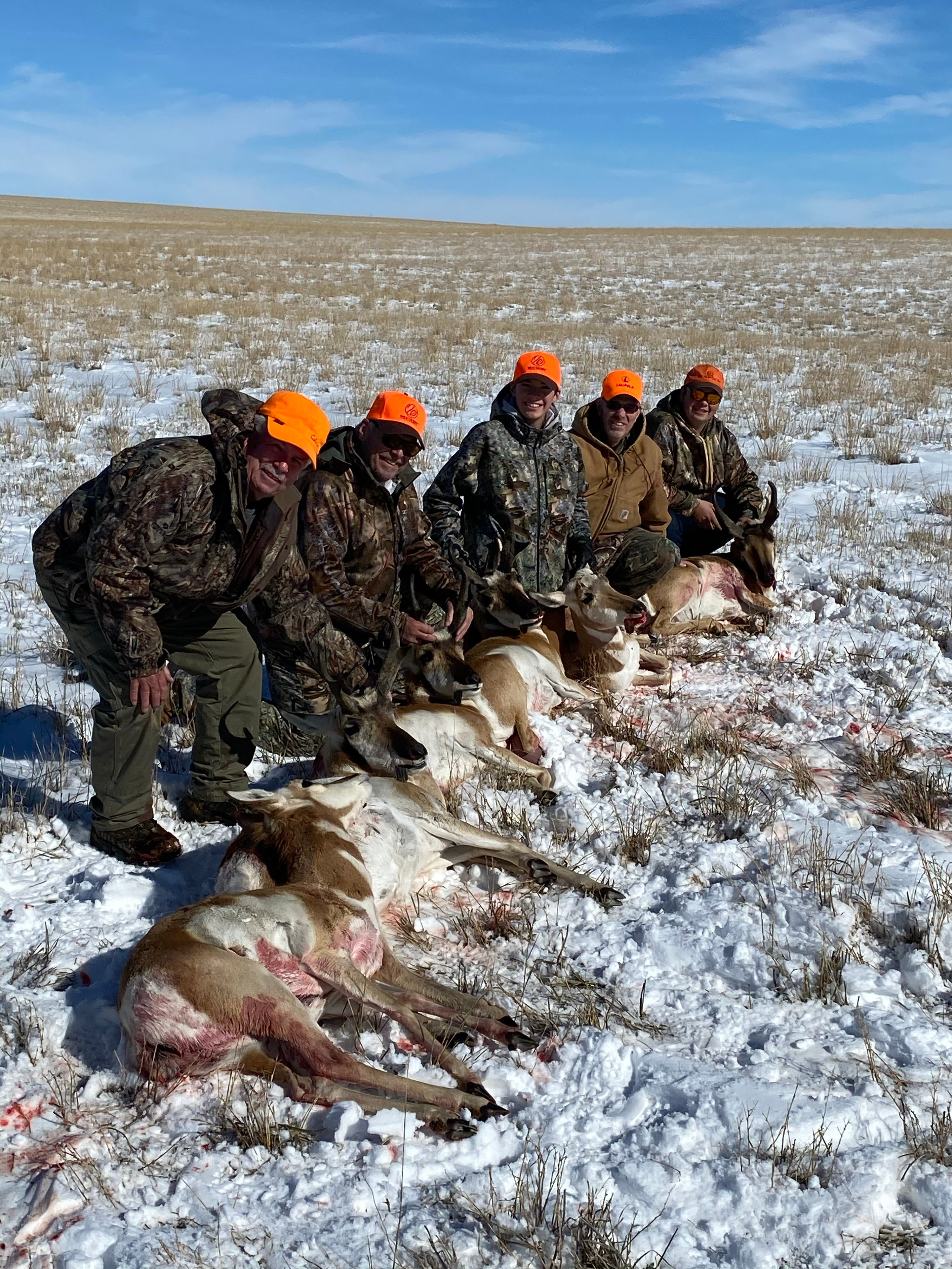 Group of hunters in blaze orange with harvested antelope in snow