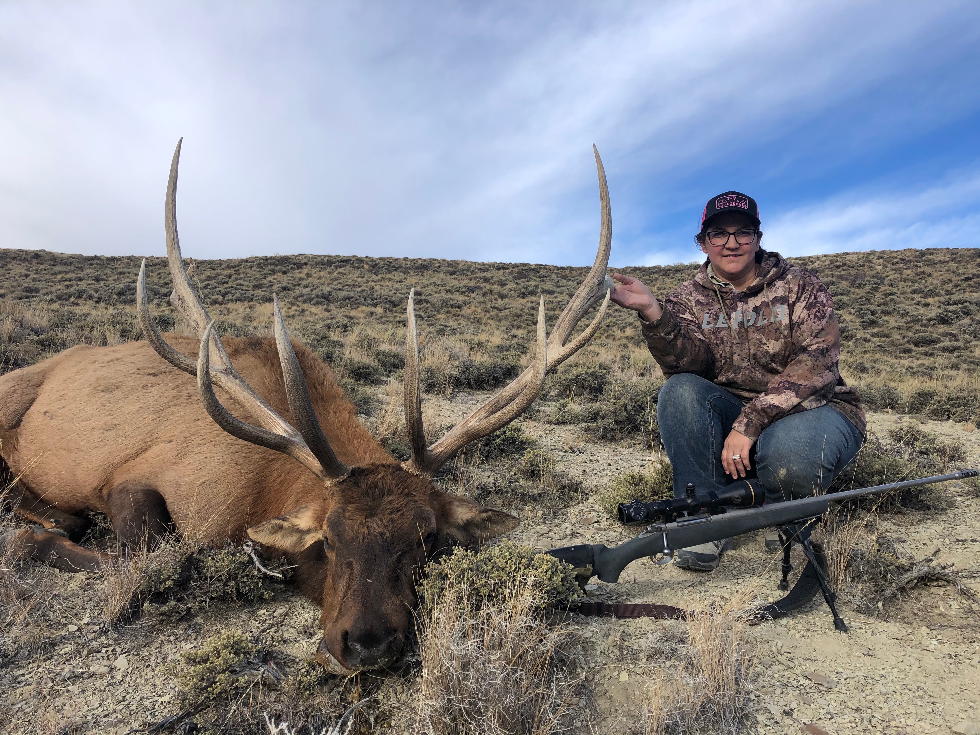 Hunter with harvested bull elk and scoped rifle on bipod