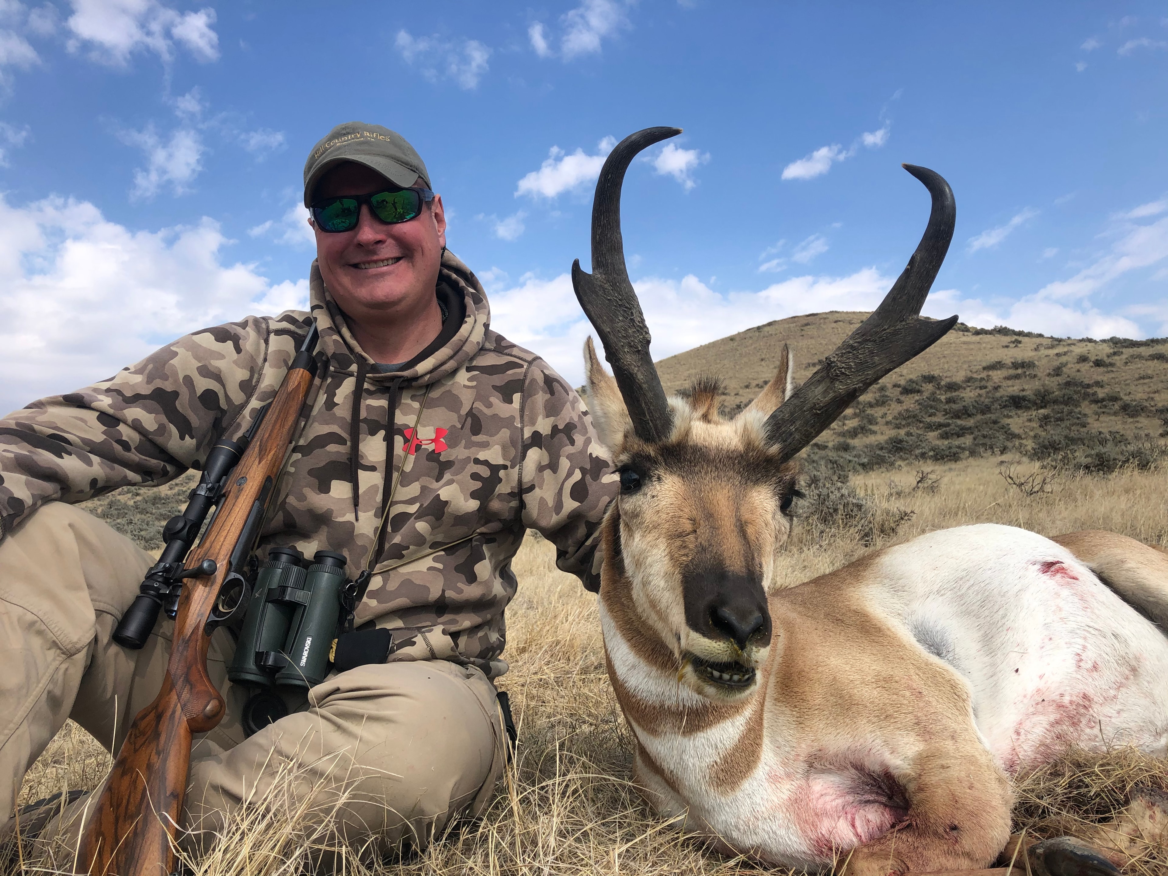 Hunter with harvested antelope buck and binoculars in sagebrush