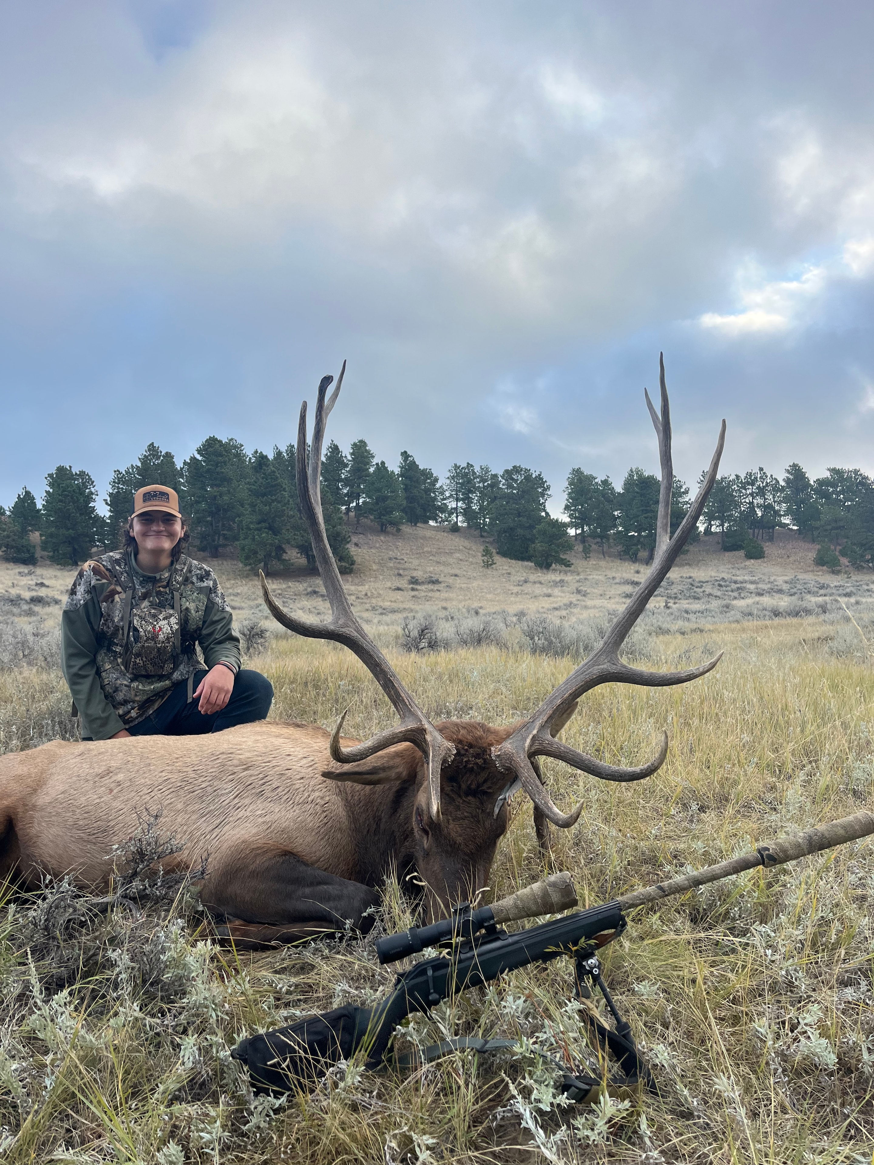 Young hunter with massive bull elk and scoped rifle on bipod in sagebrush