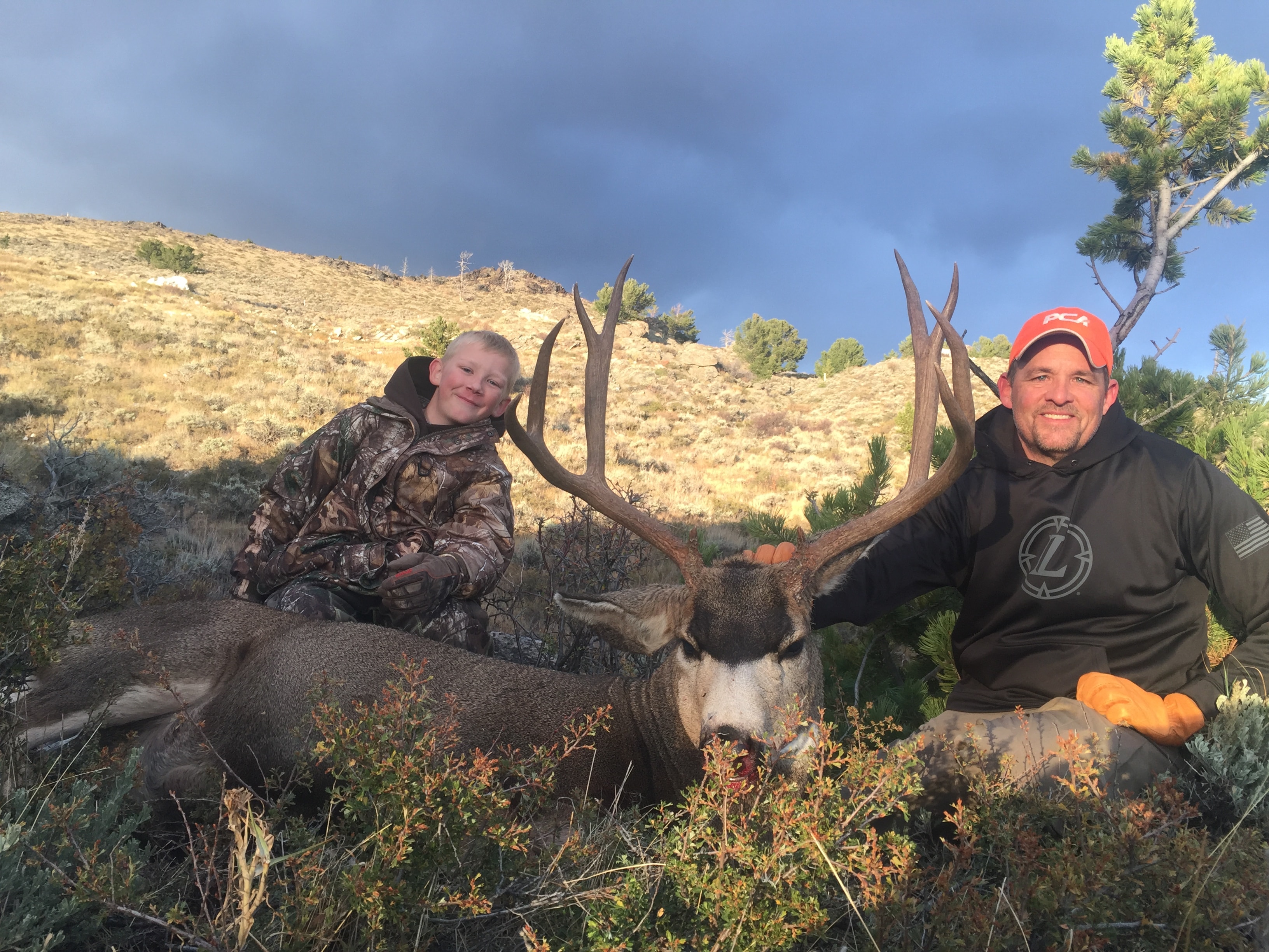 Kid and dad with harvested mule deer buck under stormy sky