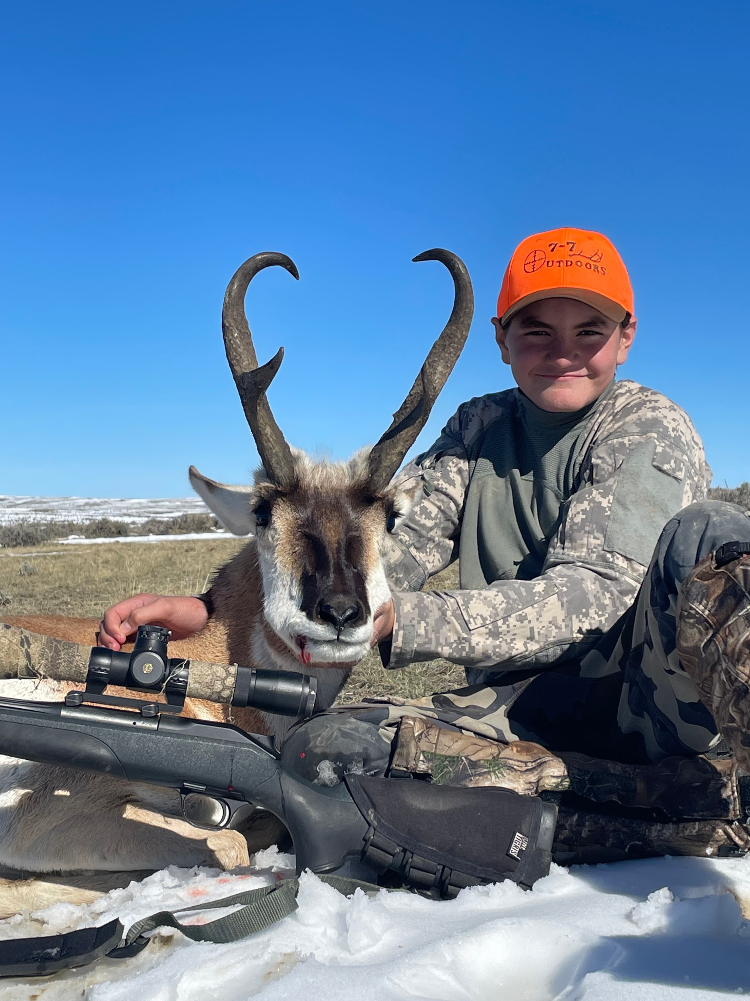 Young hunter with harvested antelope and scoped rifle in snow